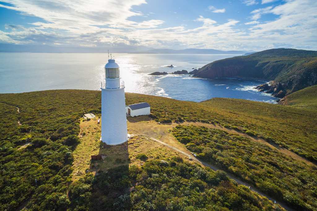 Aerial view of a white lighthouse on Bruny Island, with lush greenery surrounding it and the ocean in the background, showcasing a scenic spot included in Bruny Island day tours from Hobart.