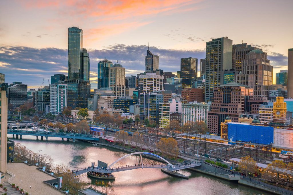 Dusk falls over Melbourne's dynamic cityscape, showing the Yarra River winding through illuminated skyscrapers and bustling streets, a vista often admired during twilight Melbourne helicopter tours.