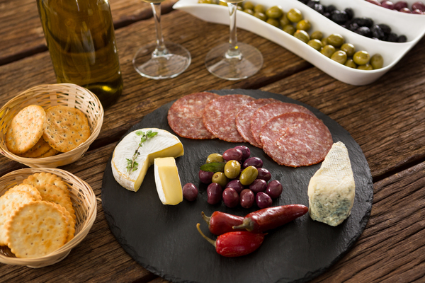 Close up photo of marinated olives with bottle of wine and food