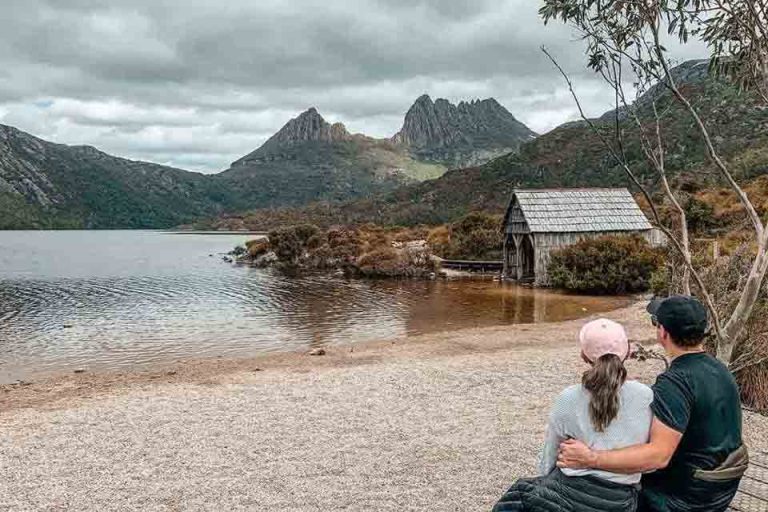 Author and husband sitting in front of the old boatshed on its shores, a romantic spot near luxury accommodations in Cradle Mountain.