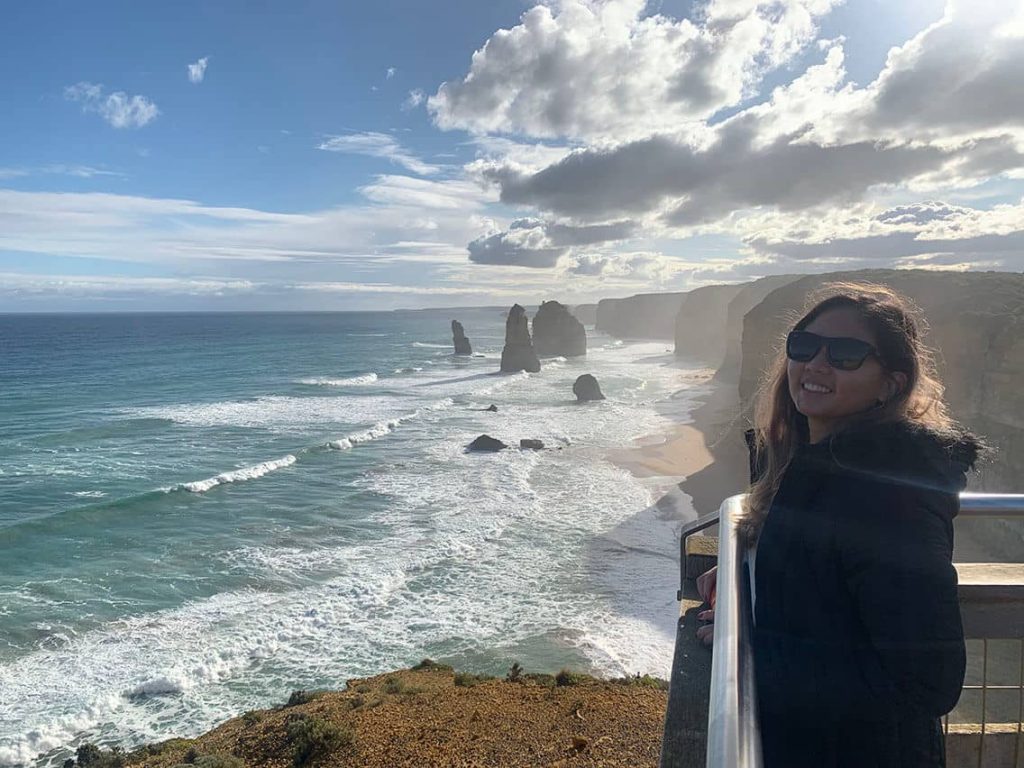 A woman standing in front of the 12 Apostles, showcasing one of the iconic landmarks that make Great Ocean Road worth visiting