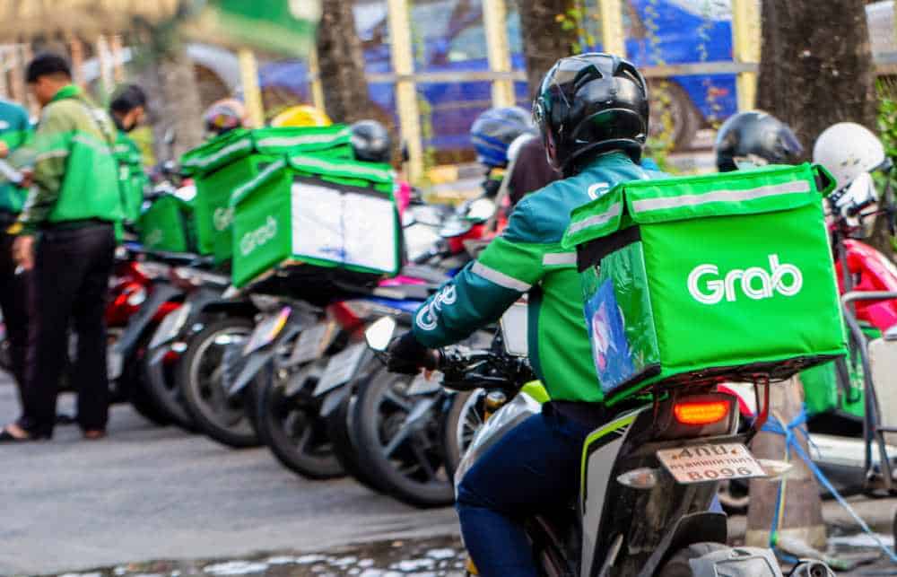 A line of GrabFood delivery riders on scooters preparing for their next delivery in Bali, highlighting the island’s vibrant food delivery scene as an extension of Grab's transport services.