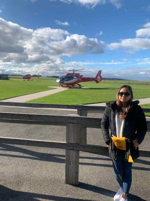 Kate standing in front of a red helicopter on a helipad, preparing for a scenic flight over the Great Ocean Road."