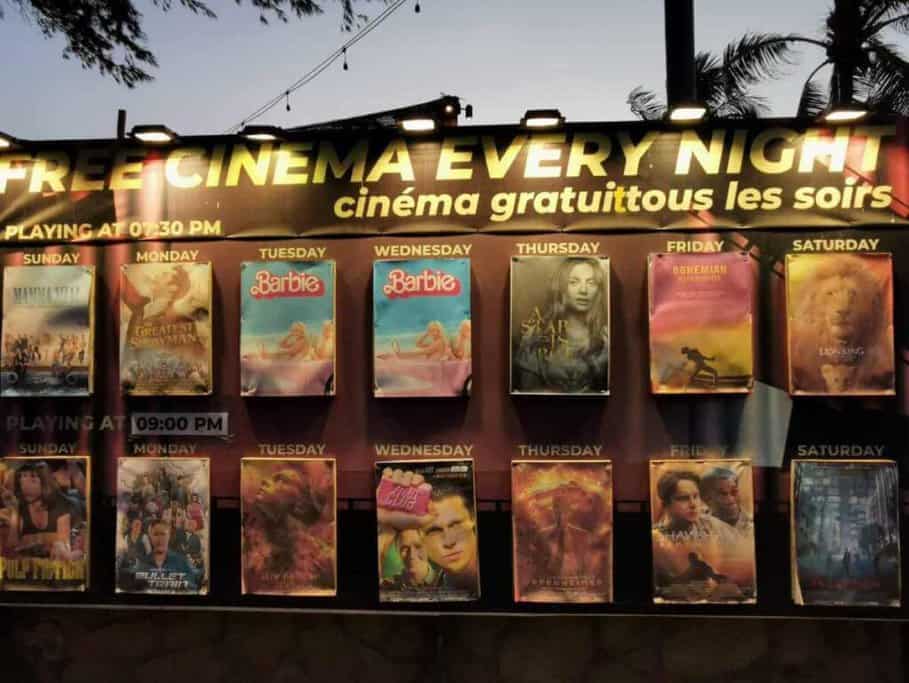 Outdoor cinema on Gili Islands featuring free nightly movie showings, including titles like 'Mamma Mia', 'The Greatest Showman', and 'The Lion King', under a twilight sky. This is one of the unique things to do in Gili Islands, offering entertainment after sunset.