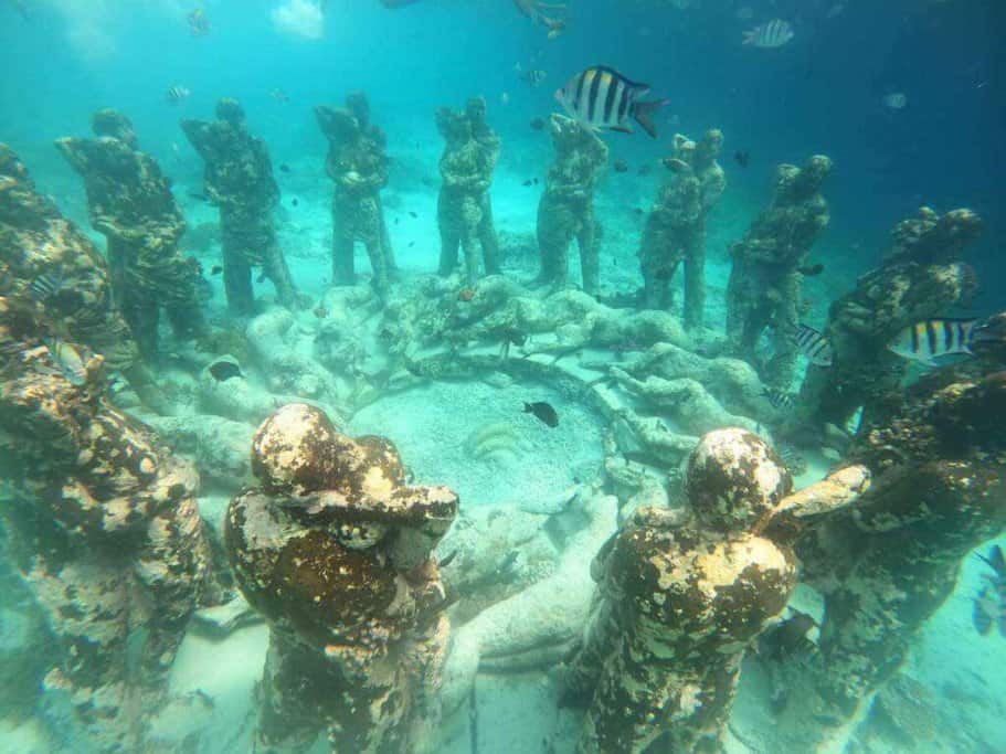 Underwater sculpture park at Gili Meno, featuring statues standing in a circle, surrounded by marine life, an enchanting diving spot among the activities to enjoy in the Gili Islands.