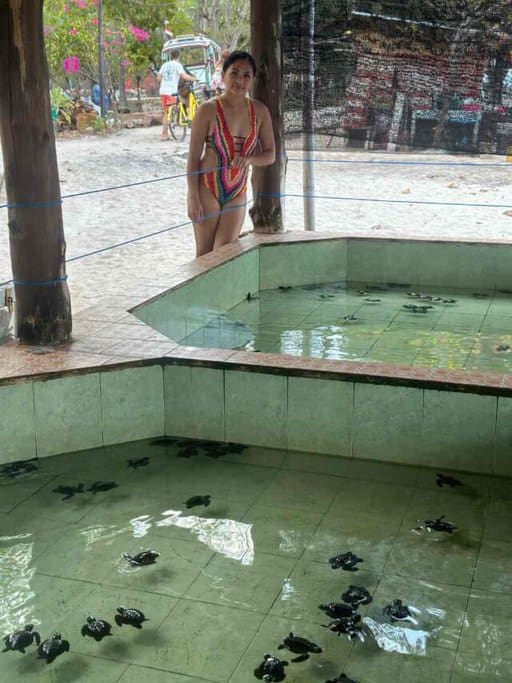 The author, Kate, stands beside a turtle hatchery pool with baby turtles in Gili Meno, highlighting the conservation efforts as one of the unique things to do in Gili Islands.