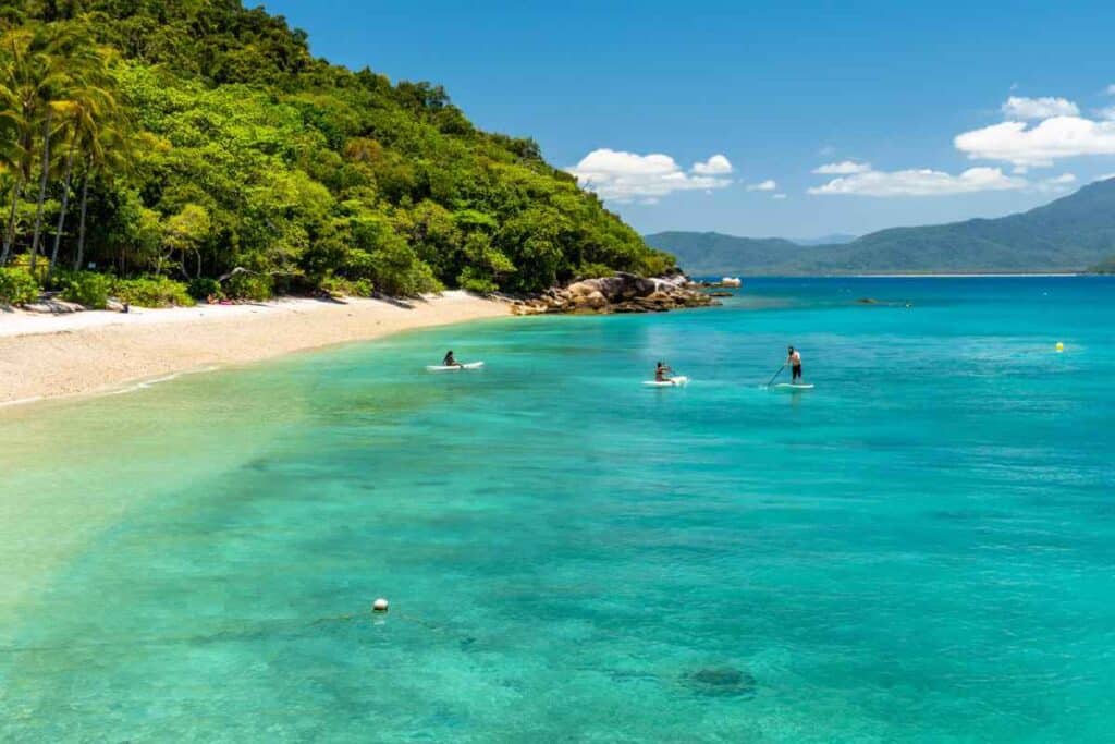 Crystal-clear waters and paddle boarders at Fitzroy Island, a tropical paradise near Cairns, showcasing the popular winter activities in Cairns for both locals and tourists seeking sunshine and sea.