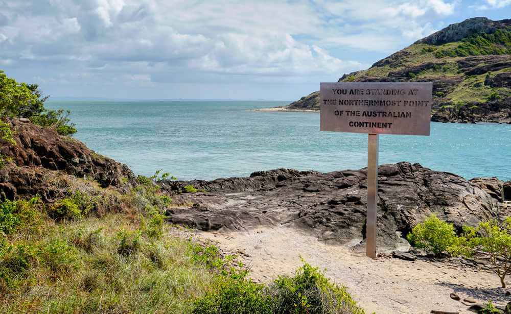 Signpost at the northernmost point of the Australian continent, a destination for adventure-seekers among the top Cairns things to do, with views of rocky shores and azure sea.