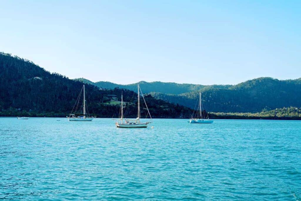 Sailboats anchored in the tranquil waters of Airlie Beach, with lush green hills in the background.