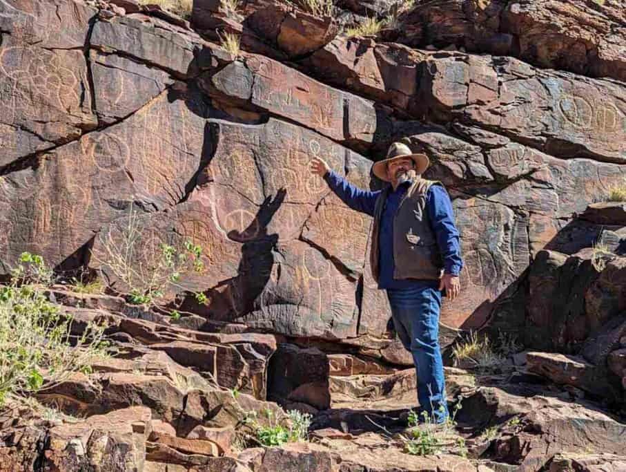 A guide points to ancient petroglyphs etched into a rocky cliff at Chambers Gorge, demonstrating the rich cultural heritage of the Adnyamathanha people. This scene is a highlight of the Flinders Ranges Tour, offering visitors an in-depth look at historical rock art and Indigenous traditions.