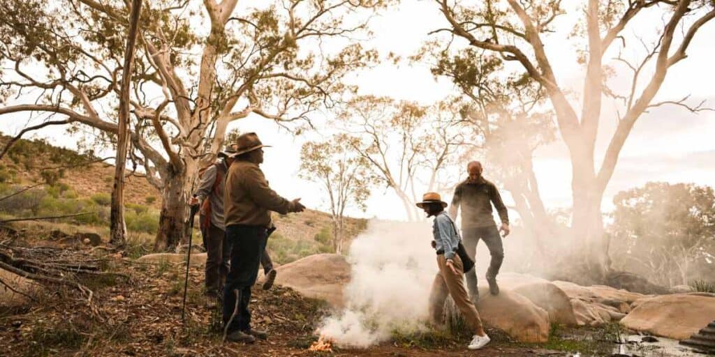 A group of people participates in a traditional smoking ceremony during the Flinders Ranges Tour, led by an Indigenous guide. This image captures the cultural immersion and spiritual connection offered on the tour, highlighting its unique and authentic experiences.