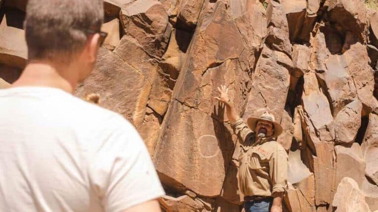 An Indigenous guide explains the significance of ancient rock carvings to a visitor during the Flinders Ranges Tour at Sacred Canyon. This image highlights the educational and cultural depth of the tour, emphasizing the connection to Adnyamathanha heritage.