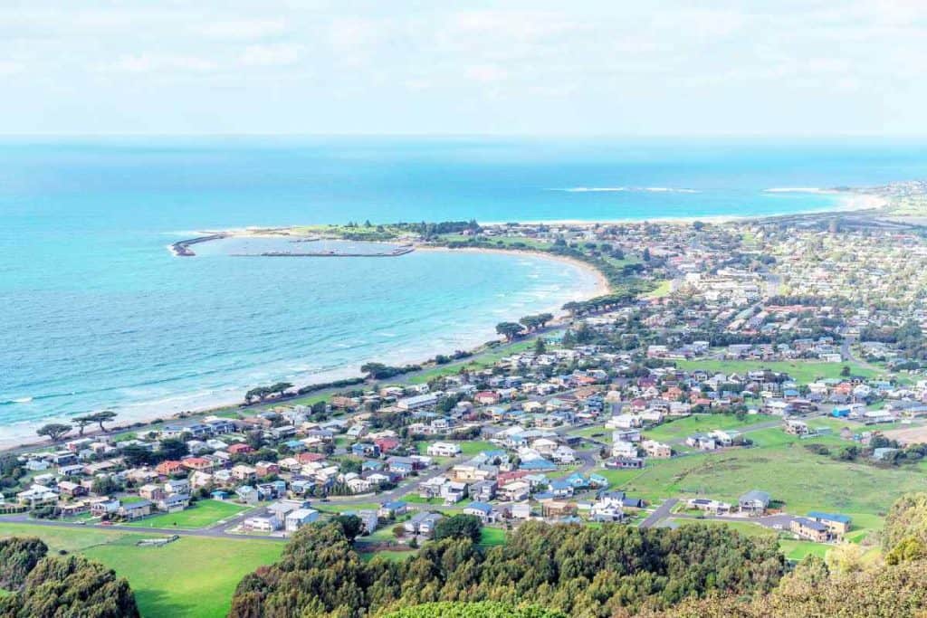 Aerial view of Apollo Bay, Australia, showcasing a coastal town with houses, lush greenery, and the ocean in the background. This image highlights one of the popular destinations for accommodation when deciding where to stay on the Great Ocean Road.