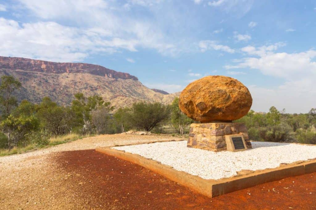 John Flynn’s Grave Historical Reserve, featuring a large boulder atop a commemorative plaque, set against the rugged landscape of the West MacDonnell Ranges, offering insights into what you need to know about Alice Springs and its rich history.