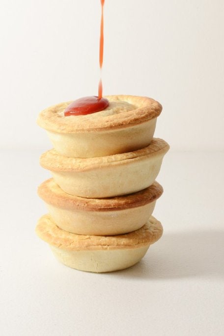 A stack of classic Australian meat pies with golden, flaky pastry, topped with tomato sauce. This savoury staple is one of the most iconic Aussie foods, loved for its rich filling and handheld convenience.