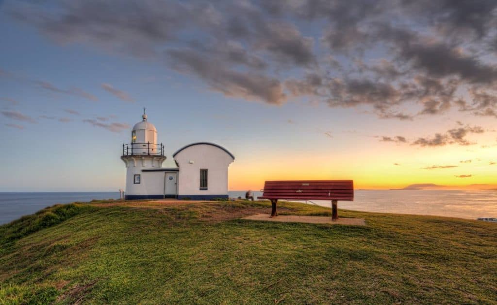 Tacking Point Lighthouse in Port Macquarie glowing at sunset with a bench overlooking the sea, a serene photo stop on the drive between Sydney and Byron Bay.