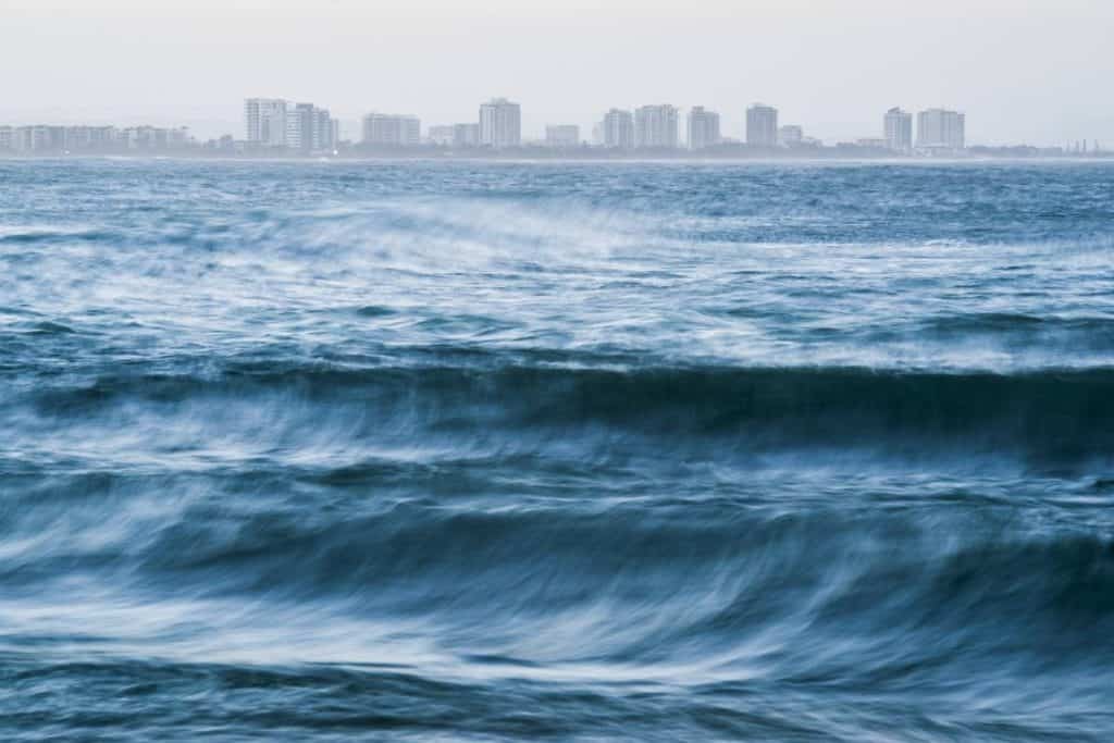 Dusk over Mooloolaba Beach with misty waves in the foreground and high-rise apartments lining the horizon, showing the coastal city vibe that’s part of the lifestyle trade-offs when weighing up the advantages and disadvantages of living on the Sunshine Coast.