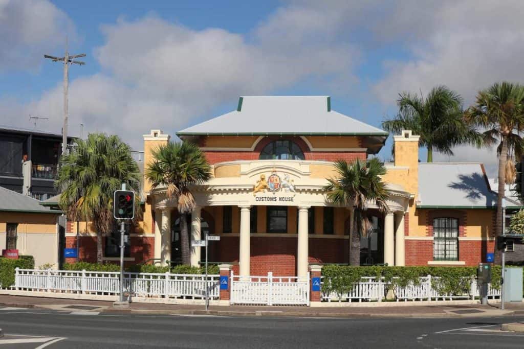 The Old Customs House in Mackay, a heritage-listed building framed by palm trees and a white picket fence, reflecting the town’s colonial past and contributing to the character often considered when weighing up the lifestyle benefits and drawbacks of living in Mackay.