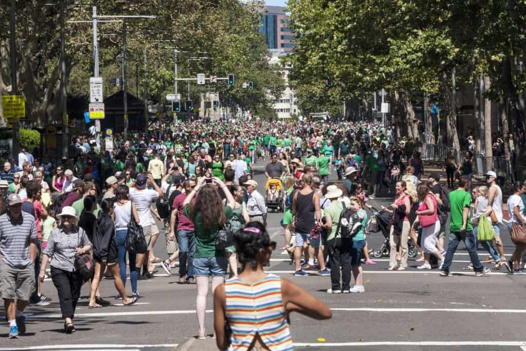 Large crowds dressed in green walking down a tree-lined city street during a festive parade, celebrating St. Patrick’s Day in Sydney as part of the annual city-wide event featured in the blog post.