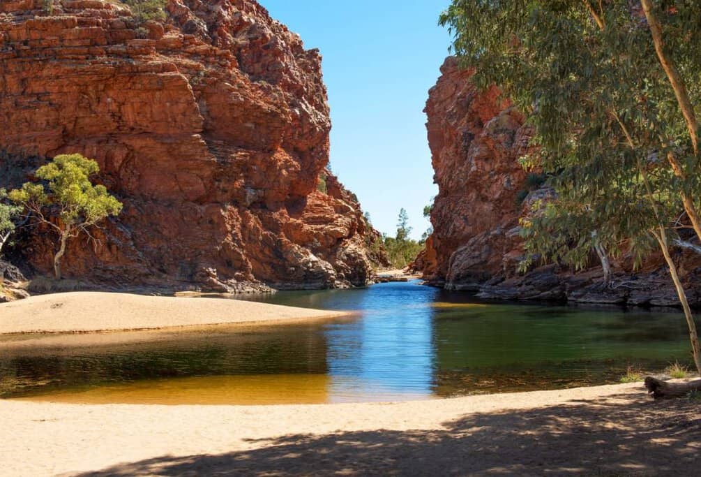 Calm waterhole at Ellery Creek Big Hole framed by towering red rock cliffs and sandy banks, showcasing a unique inland spot often included among Australia’s top coastal and river beaches.