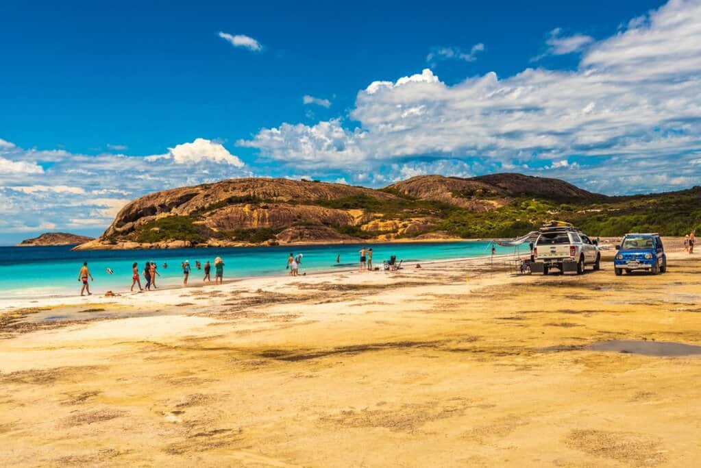People swimming and relaxing on the white sand at Hellfire Bay with turquoise water and rugged granite hills in the background, highlighting one of the top-rated beaches in Australia featured in the Australia’s Best Beaches guide.