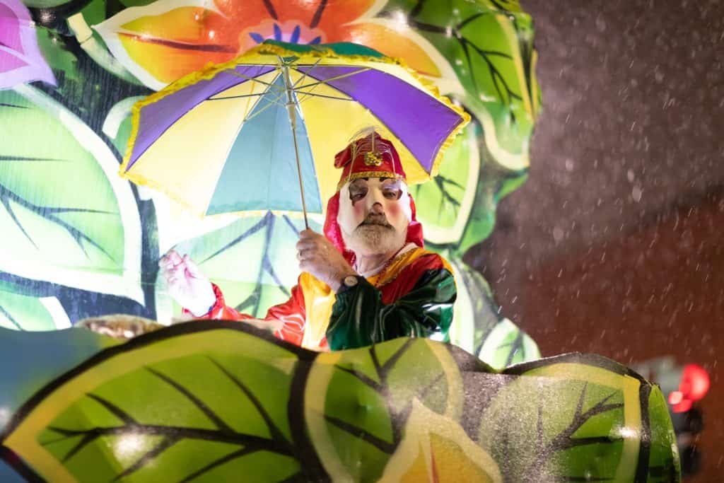 Performer in colourful costume holding a rainbow umbrella on a parade float in the rain during Sydney Mardi Gras 2026 celebrations in Sydney city at night