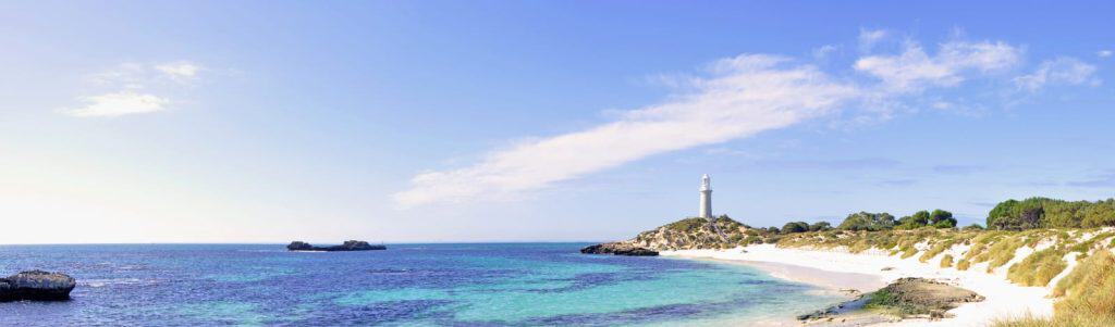 Clear turquoise water and soft white sand at Pinky Beach with a lighthouse standing on the headland, capturing the coastal beauty that makes it one of Australia’s top beaches featured in the guide Best Beaches in Australia.