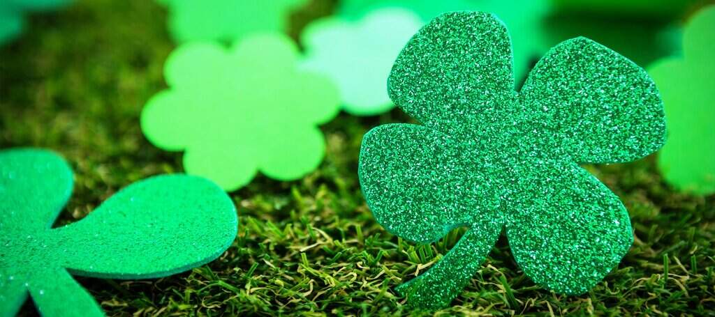 Close-up of green glitter shamrocks resting on grass, symbolising Irish luck and the festive decorations seen during St. Patrick’s Day.