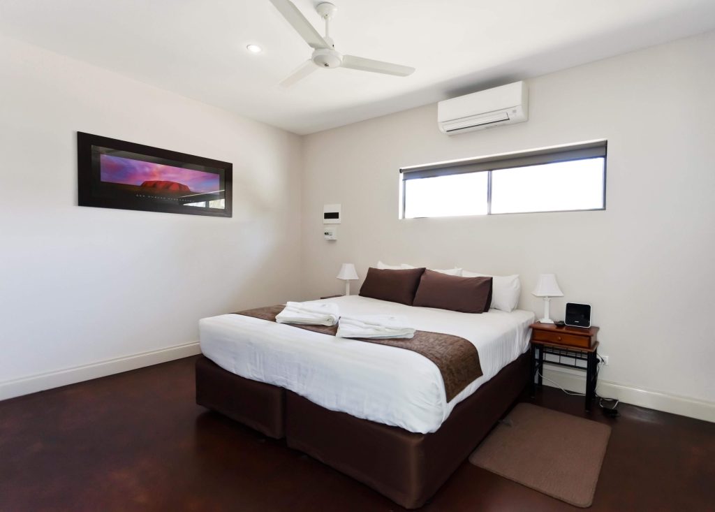 Modern apartment bedroom in Alice Springs with a queen bed, bedside tables, ceiling fan, and air conditioning, offering a self-contained option for travellers comparing apartments and deciding where to stay in Alice Springs NT.