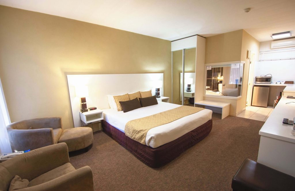 Comfortable motel room in Alice Springs featuring a queen bed, armchairs, mirrored wardrobe, and kitchenette facilities, ideal for travellers looking for affordable places to stay in Alice Springs near the town centre.