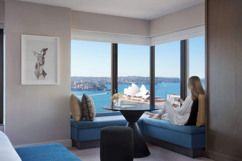 A woman relaxing by the window seat at Four Seasons Hotel Sydney in Circular Quay, enjoying sweeping views of the Sydney Opera House and harbour, one of the best luxury hotels in Sydney with harbour views.