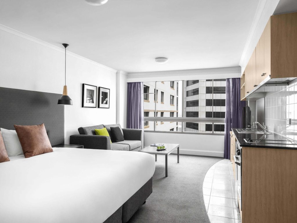 A modern studio room at Mantra on Kent hotel in Sydney CBD, one of the best budget-friendly options for where to stay in Sydney, featuring a king bed, kitchenette, and city views.