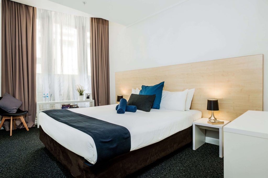 Simple modern hostel room with double bed and bright window at Nomads Sydney in the city centre, highlighting budget hotels in Sydney and affordable Sydney CBD hotels for travellers near major attractions