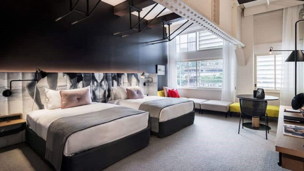 Industrial-style hotel room with two beds and large windows at Ovolo Sydney Woolloomooloo near Sydney Harbour, showcasing a stylish option for travellers deciding where to stay in Sydney close to major harbour attractions