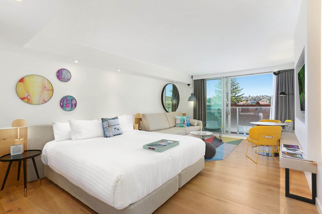 Bright modern hotel room with balcony and seating area at QT Bondi near the beach, highlighting stylish Bondi Beach accommodation in one of the best areas to stay in Sydney for coastal views and relaxed neighbourhood vibes