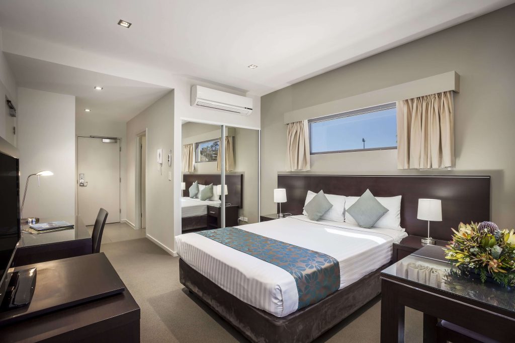 Modern serviced apartment in Alice Springs with a queen bed, bedside lamps, work desk, mirrored wardrobe, and air conditioning, ideal for travellers comparing accommodation in Alice Springs and deciding where to stay in Alice Springs NT.