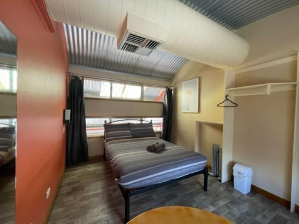 Private hostel room in Alice Springs with a double bed, open wardrobe, timber floors, and large window, highlighting a budget-friendly option for travellers planning where to stay in Alice Springs Australia.
