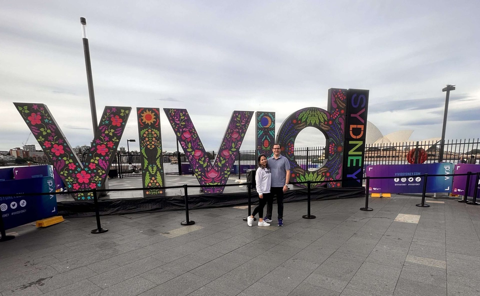 Colourful Vivid Sydney sign display at the harbour with visitors posing in front, capturing the vibrant atmosphere of Vivid Sydney and its iconic light installations.