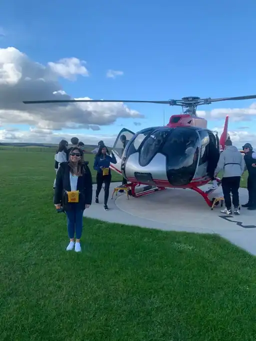 Traveler stands beside a helicopter on a grassy helipad before a scenic flight over the Great Ocean Road.