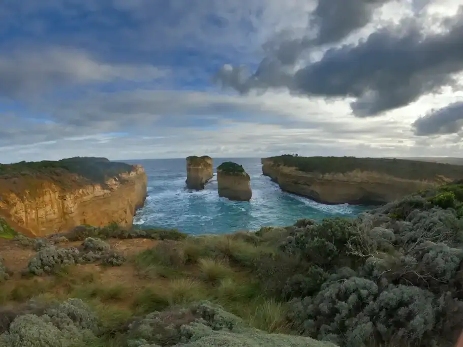 View of Island Arch along the Great Ocean Road, with two limestone rock stacks rising from turquoise water between towering coastal cliffs.