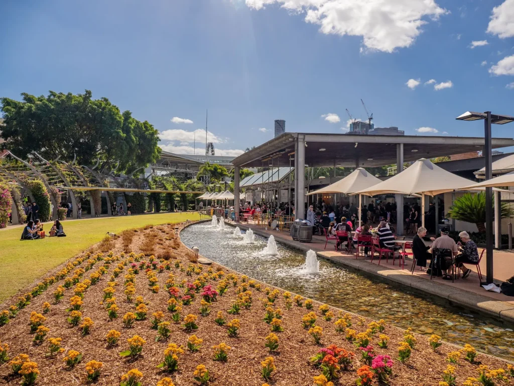 Colourful flower beds and a long fountain beside a busy outdoor cafe at the Brisbane City Botanic Gardens. Exploring the gardens is one of the relaxing things to do in Brisbane on a sunny day.