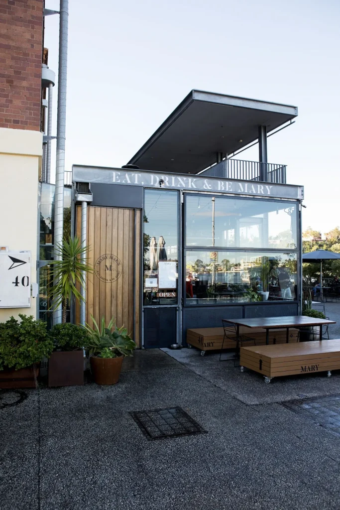 Riverside entrance to Brisbane Powerhouse with outdoor seating and the words "EAT. DRINK & BE MARY" displayed above Mary Maes restaurant. Brisbane Powerhouse is one of the citys cultural attractions with dining and entertainment in a converted industrial building.