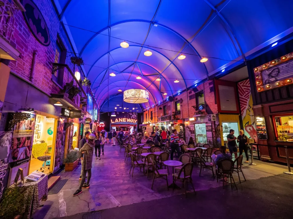 Colourful covered laneway at Eat Street Northshore filled with food stalls and outdoor tables under glowing blue and purple lights. Visiting the lively food market is a fun Brisbane activity for an evening itinerary.