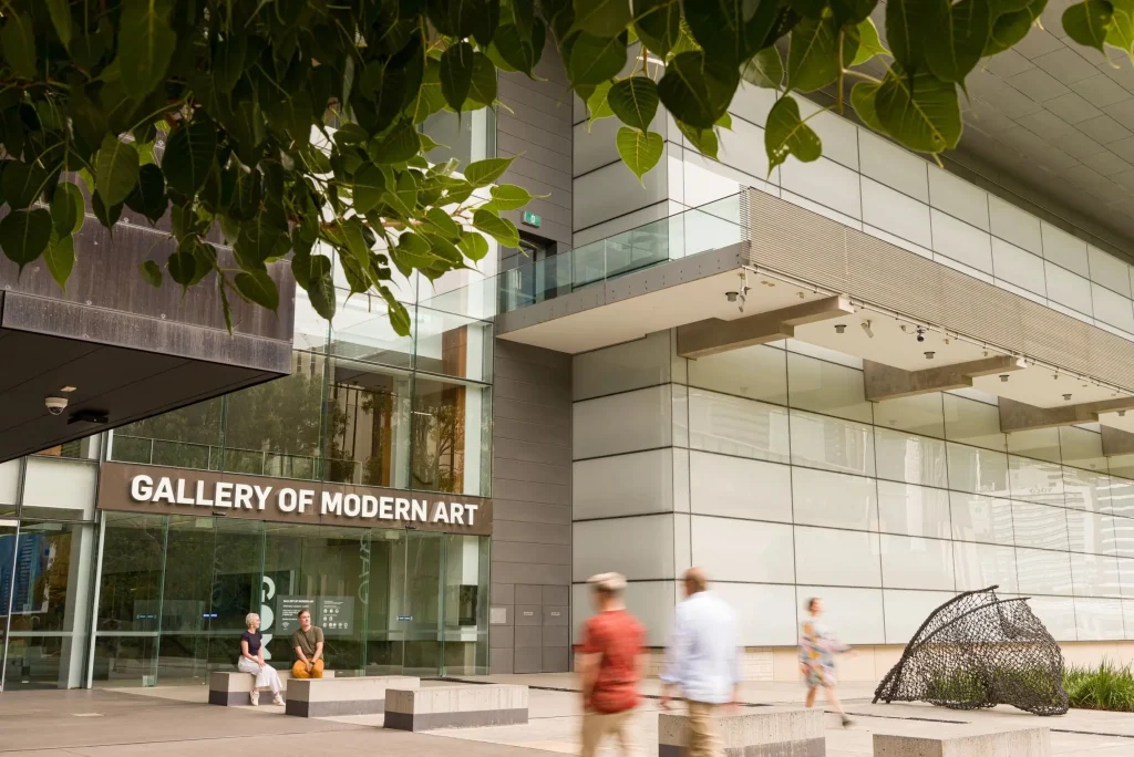 Gallery of Modern Art entrance in Brisbane with visitors walking past the contemporary building beneath leafy trees. The gallery is a popular Brisbane activity for art lovers exploring the city.