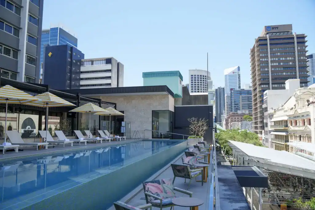Hyatt Regency Brisbane rooftop pool lined with sun loungers and yellow striped umbrellas overlooking the surrounding city buildings. The elevated pool deck provides a sunny place to swim and relax in central Brisbane.