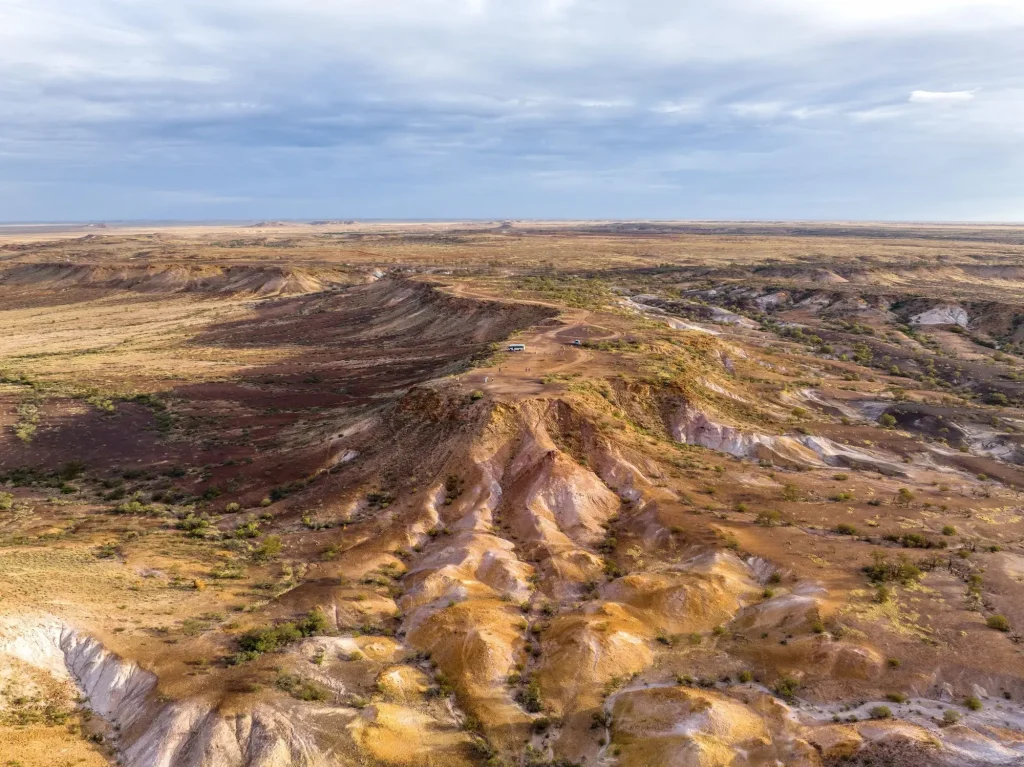 Sweeping view across the colourful red brown and pale yellow ridges of Kanku Breakaways National Park beneath a cloudy sky. Visiting this dramatic outback landscape is one of the top Coober Pedy activities.