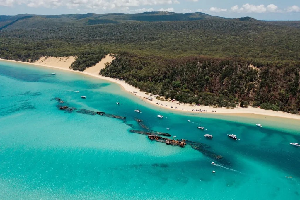 Aerial view of Moreton Island with turquoise water surrounding the Tangalooma Wrecks and boats anchored beside a long sandy beach. A Moreton Island day trip is a popular way to extend a Brisbane itinerary beyond the city.