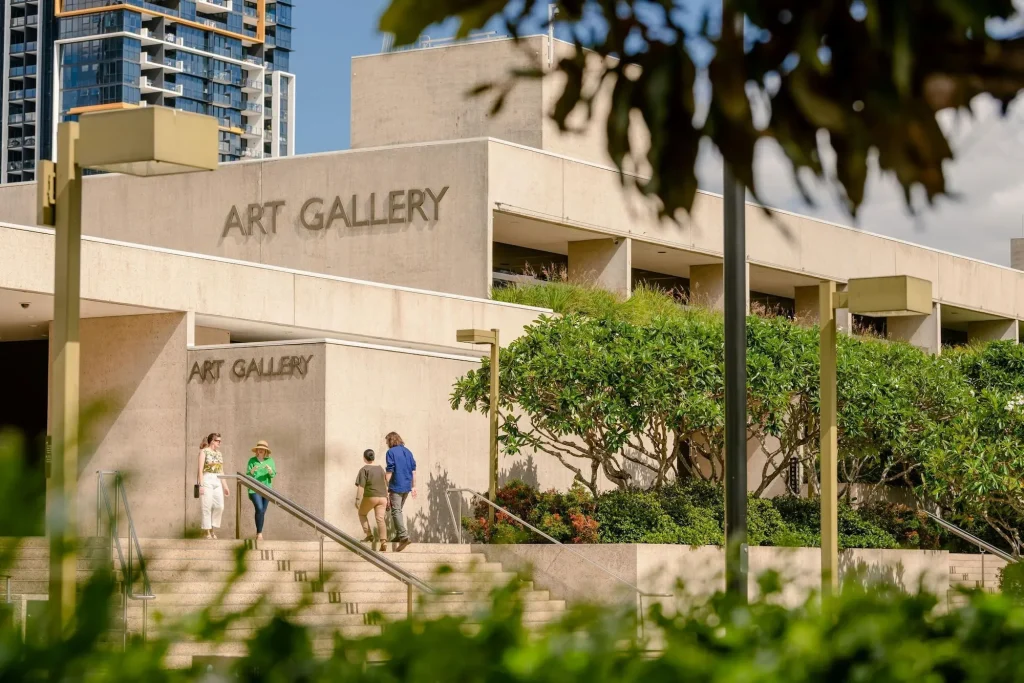 Visitors walking up the steps to the Queensland Art Gallery in Brisbane surrounded by leafy gardens and modern city buildings. Visiting the gallery is one of the best things to do in Brisbane for art and culture.