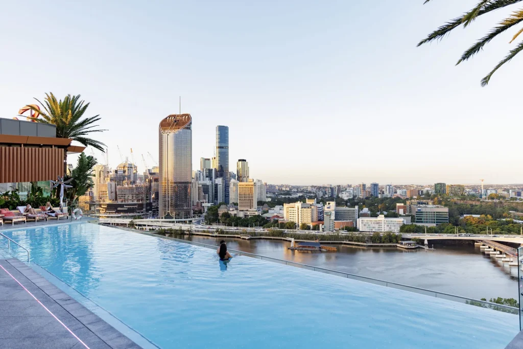 The Emporium Hotel rooftop infinity pool overlooking the Brisbane River and city skyline. Guests swim and relax beside the water with panoramic views across Brisbane.
