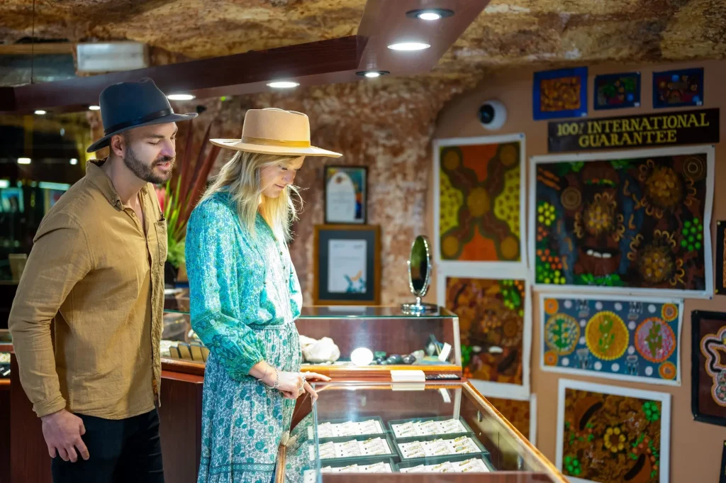 Two visitors browse opal jewellery in glass display cases inside the underground Umoona Opal Mine. Exploring an opal mine is one of the quintessential Coober Pedy activities.